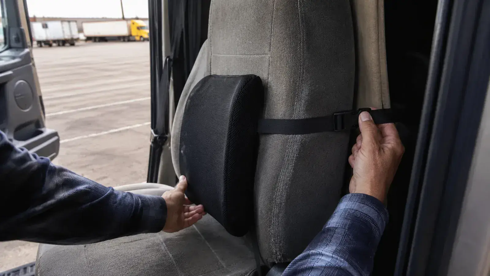 Close-up of hands adjusting the strap of a black mesh lumbar support pillow around a truck seat back