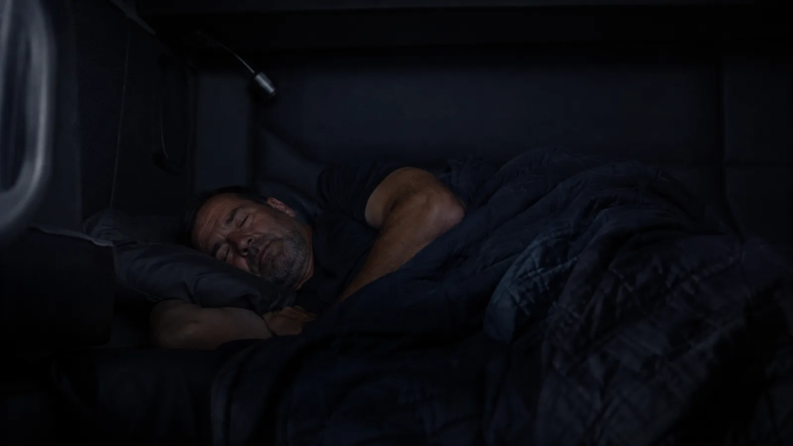A truck driver sleeping soundly in a fully darkened sleeper cab bunk