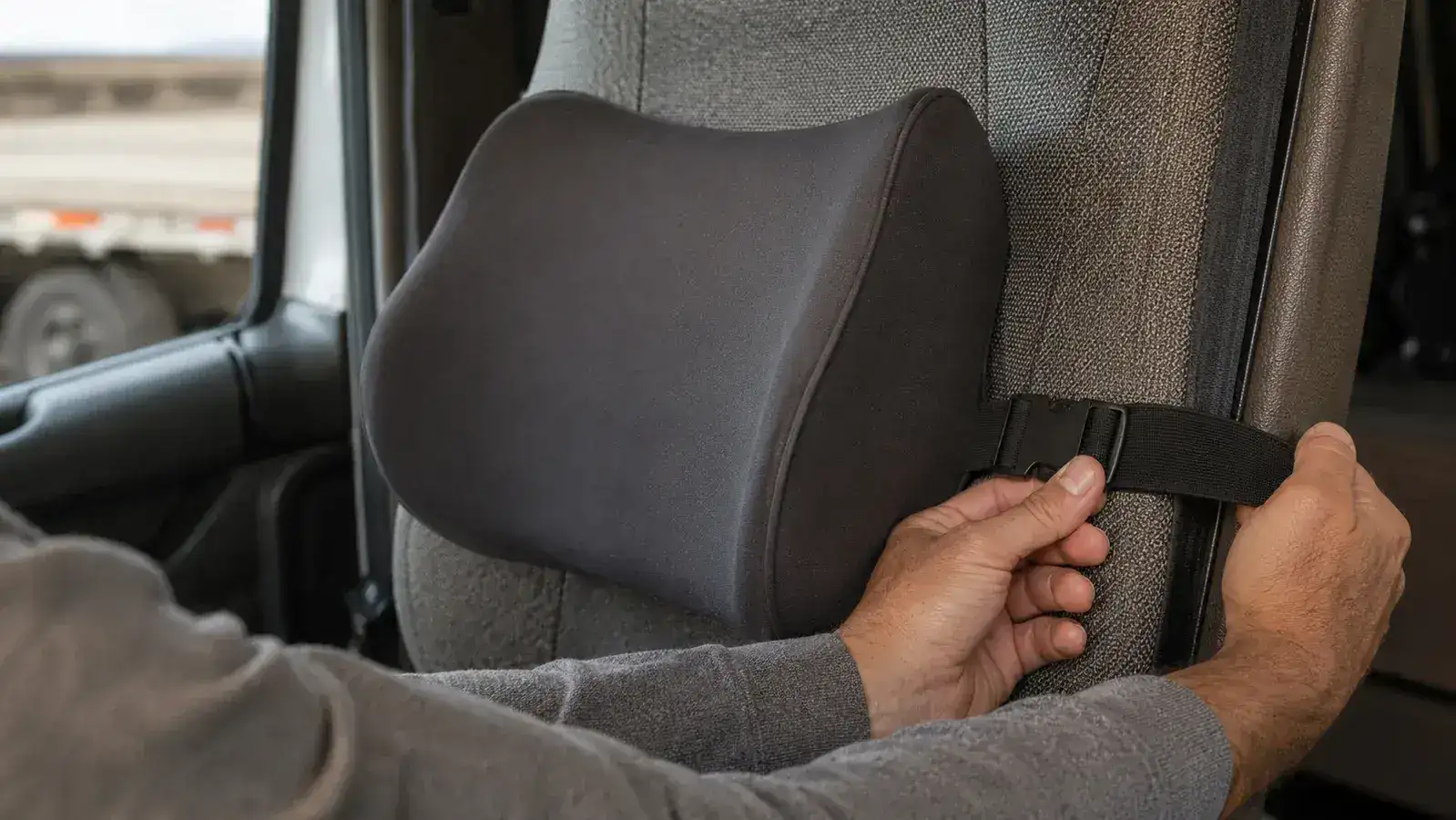 Close-up of hands re-cinching the elastic strap of a memory foam lumbar pillow around a truck seat headrest post