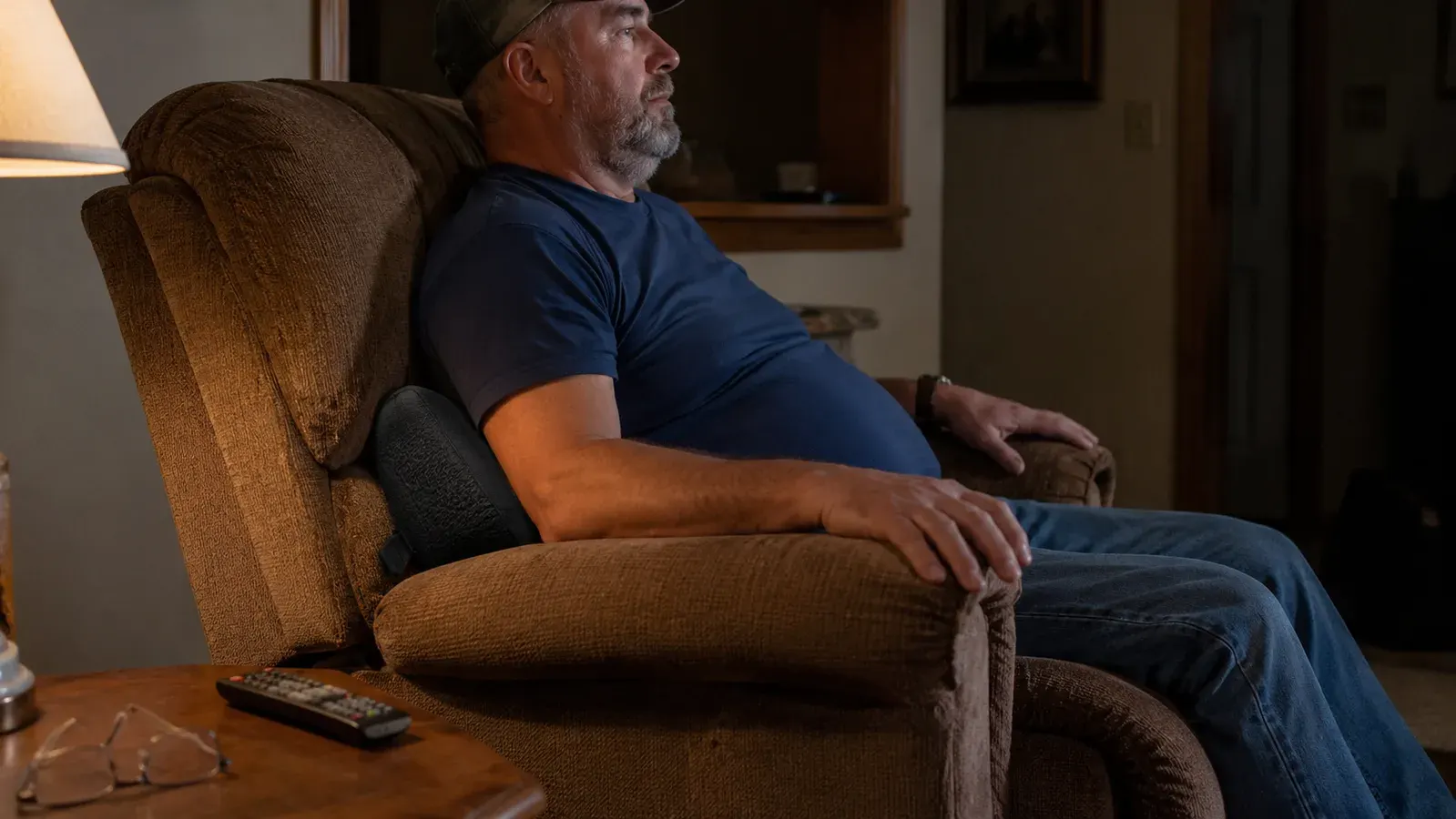 Man leaning back into a black lumbar support pillow set into a brown recliner in a living room