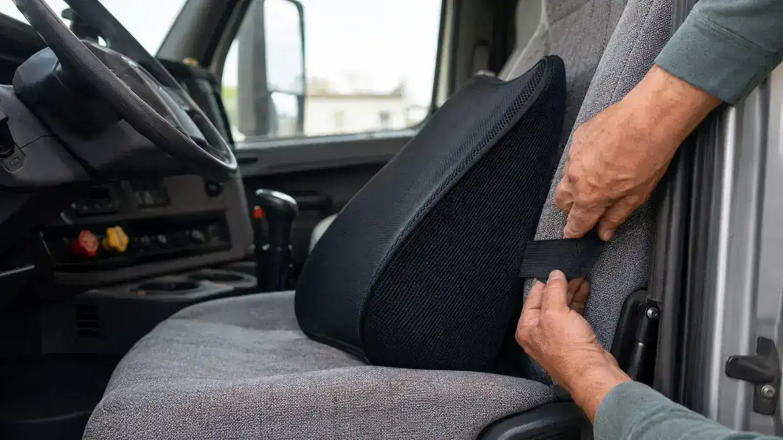Hands strapping the Everlasting Comfort black mesh lumbar pillow to a truck seat backrest