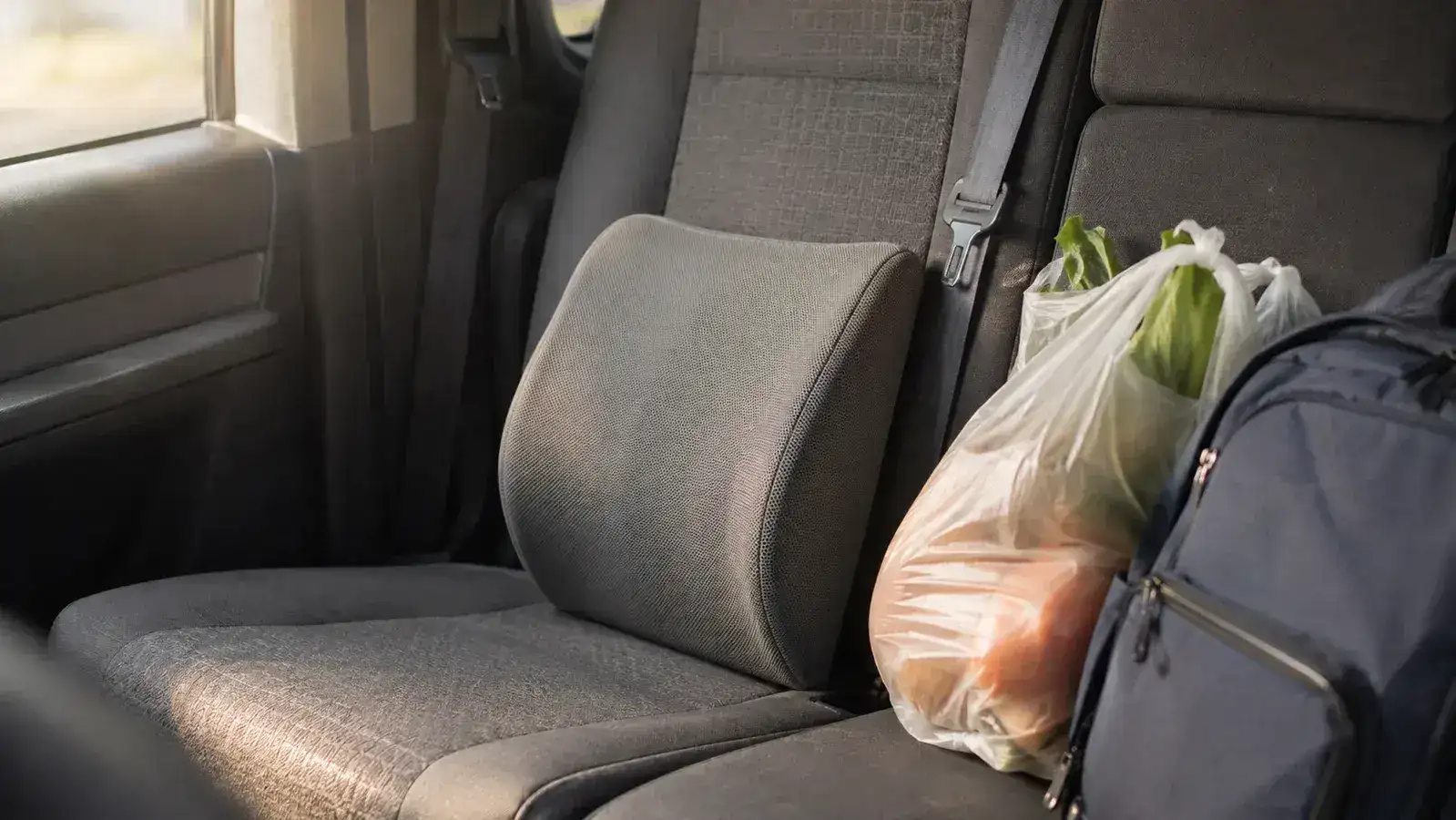 An unbranded gray lumbar pillow sitting on the back seat of a minivan next to grocery bags