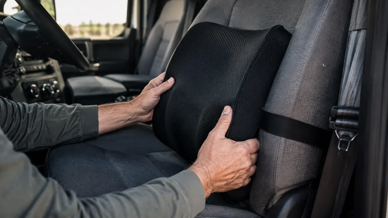 Close up of hands positioning an Everlasting Comfort memory foam lumbar support pillow against the low curve of a truck seat back