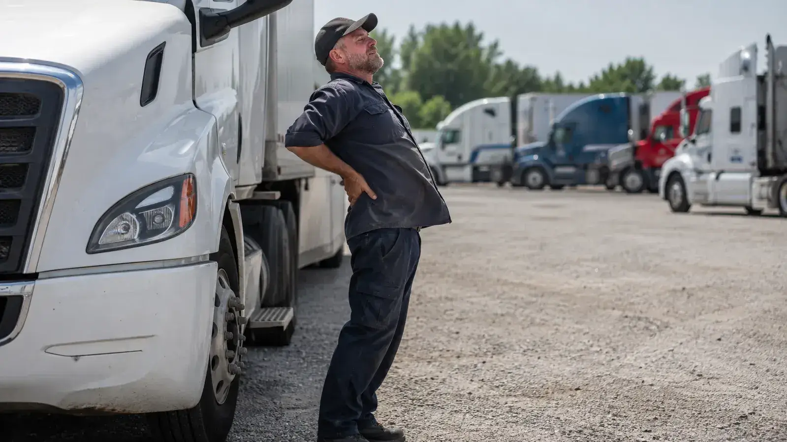 Truck driver standing beside his rig at a rest stop stretching his lower back during a break