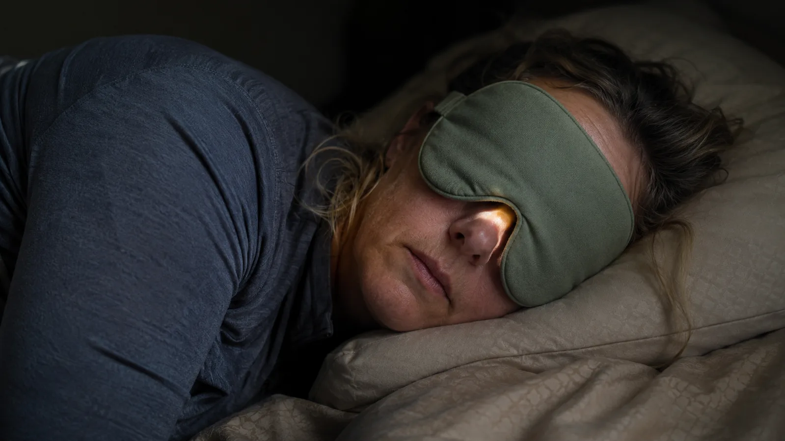 Woman's face shown from the side wearing a weighted sleep mask with a small gap of light visible near the bridge of her nose