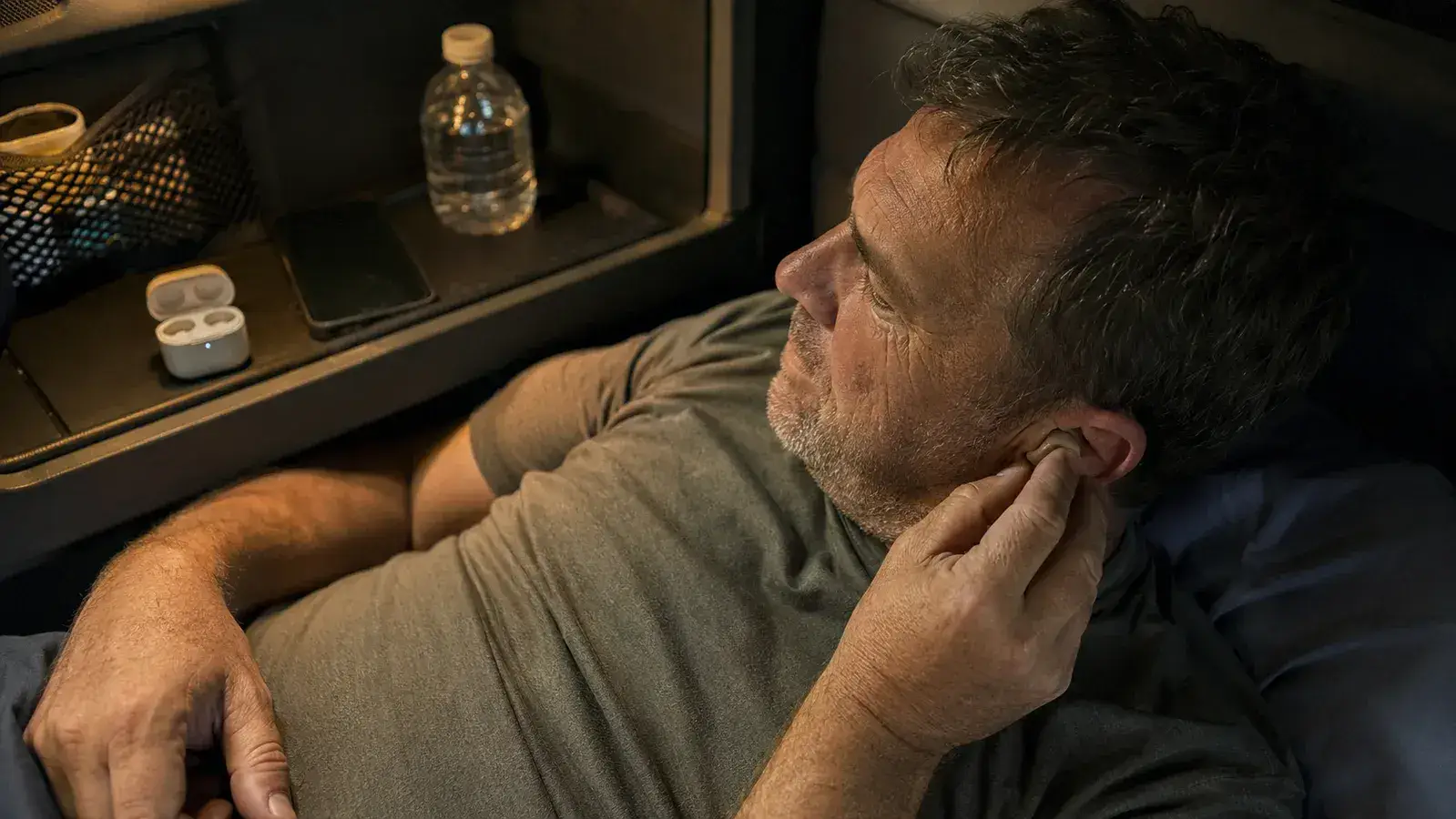 A truck driver inserting a small sunvito silicone sleep earbud into his ear while lying in a sleeper cab bunk.